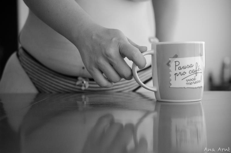 auto-retrato. imagem recortada, aparece minha mão, segurando uma caneca, escrito "pausa pro café, você merece". Ao fundo, desfocado, aparece meu corpo.